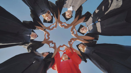 A group of seven college graduates make a heart shape from their hands while standing in a circle wearing robes.の写真素材