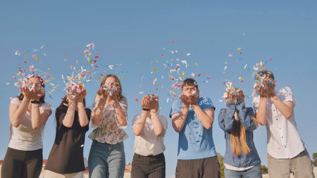 Friends blow colorful paper confetti on a sunny day.の写真素材
