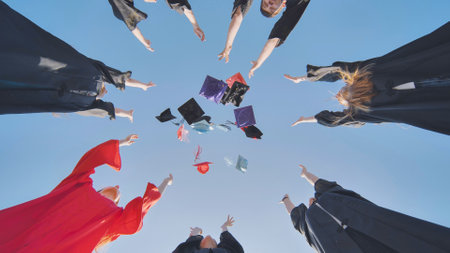 Happy college graduates standing in a circle tossing colorful hats up.の写真素材