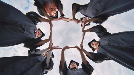 College graduates in black robes make the shape of a square from their hands.