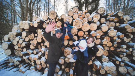 Young family in winter against the background of logs in the woods.の写真素材