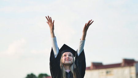 Joyful girl student graduates with her hands in the air.