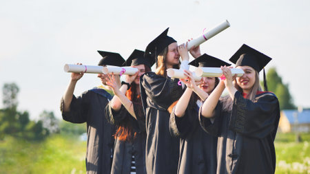 Cheerful graduates on a sunny day look through diplomas like a telescope.の写真素材