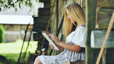 Village Slavic girl flipping a tablet in the countryside by the barn.の写真素材