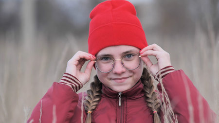 Portrait of a teenage girl in glasses standing in tall grass in the fall.