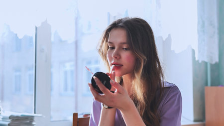 A long-haired schoolgirl paints her lips with a mirror in the classroom.の写真素材