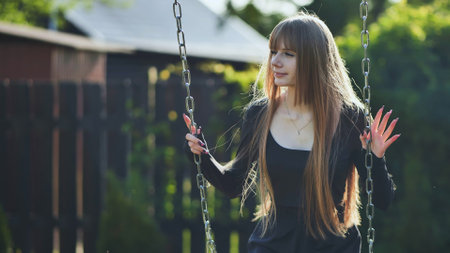 A blonde-haired girl in a black dress rides on a swing.の写真素材