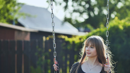 A blonde-haired girl in a black dress rides on a swing.の写真素材
