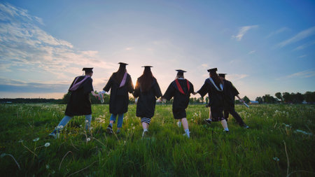 Six graduates in robes walk against the backdrop of the sunset.の写真素材