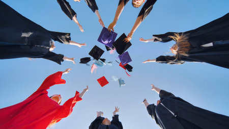 Graduates tossing multicolored hats against a blue sky.の写真素材