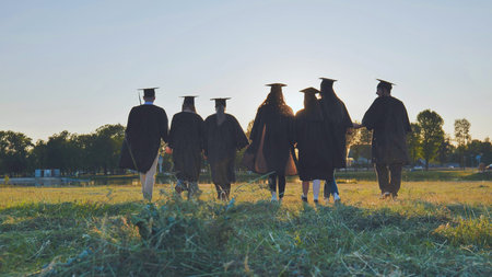 College graduates walk at sunset holding hands.