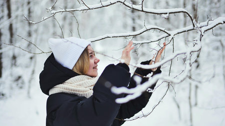 A girl gently touches snowy tree branches in the forest.の写真素材