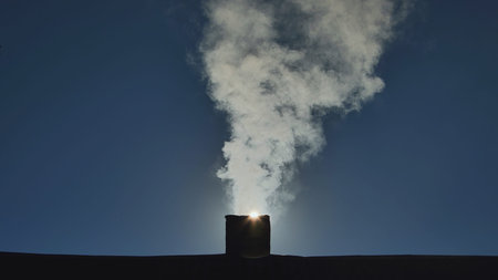 Silhouette of smoke against the sun from the chimney of a village house.の写真素材