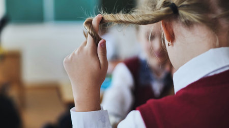 A girl touches a braid of her hair during class.