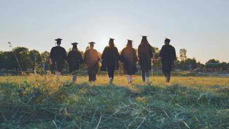 College graduates walk at sunset holding hands.