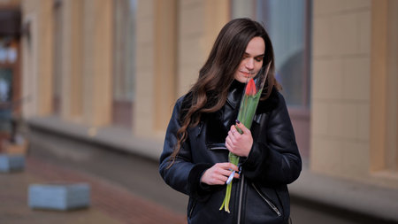 Portrait of a happy brunette girl with a tulip in the background of the city in the cold season.