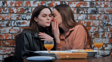 Two young girls gossiping sitting in a cafe.