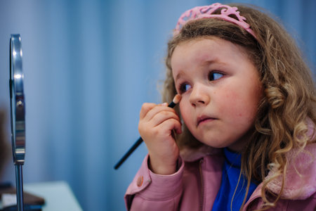 Little girl wearing a pink tiara applying makeup using a brushの写真素材