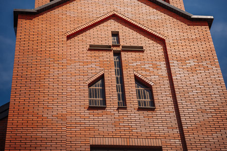 Warm sunlight illuminating a red brick wall of a modern church with a cross and windowsの写真素材