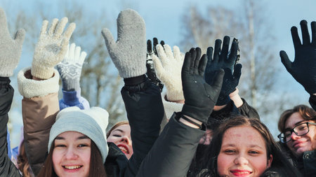 New Year and Christmas concept. School friends raise their hands with mittens up in the park in...