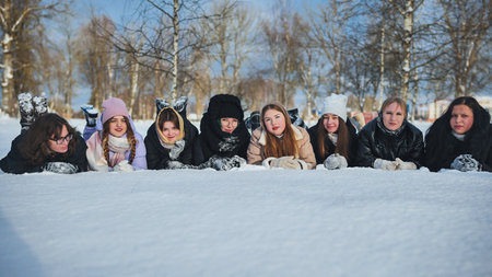 School friends lie in the snow and sprinkle snow on each other.