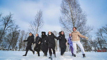 Friends holding hands running towards each other in the snow on a sunny day.の写真素材
