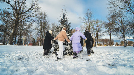School friends run around the spruce tree holding hands. Christmas concept.