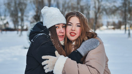 Two young girls are hugging in a winter park on a snowy day, demonstrating their friendship and camaraderieの写真素材