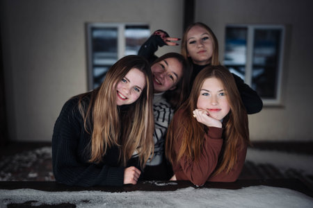 Four happy schoolgirls posing on a snow covered table during a winter photo shoot, having fun togetherの写真素材
