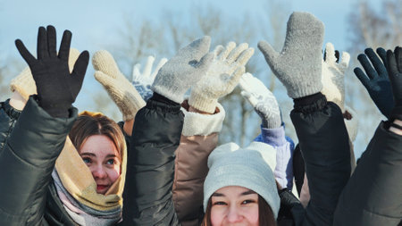 Schoolgirls in gloves happily raising their hands on a sunny winter day, enjoying outdoor activities togetherの写真素材
