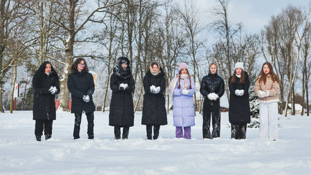 Group of schoolgirls holding snowballs, enjoying a winter day in a snowy park, ready for a snowball...