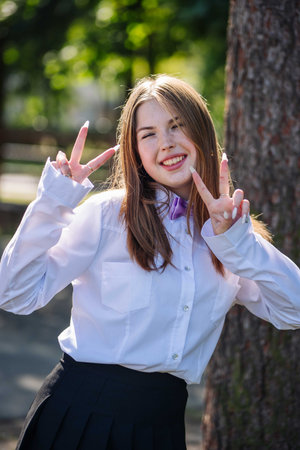 Happy student wearing white shirt and black skirt showing victory sign with both hands on first...