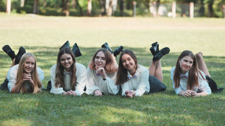 Five happy students in white shirts and bow ties are lying on the grass in a park, enjoying a sunny dayの写真素材