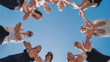 High school students joining hands in a circle under a clear blue sky, representing teamwork and solidarityの写真素材