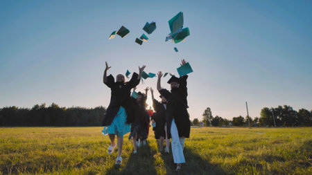 Graduates running in a field, throwing their diplomas in the air, celebrating the end of high schoolの写真素材