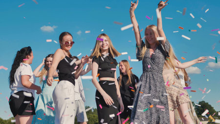 High school graduates joyfully tossing colorful confetti under a clear blue skyの写真素材