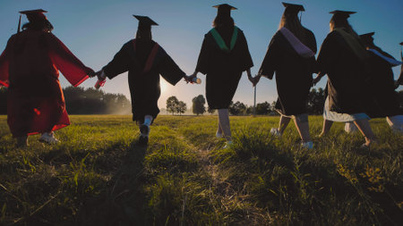 Students in graduation gowns joyfully running through a field at sunset to celebrate their academic successの写真素材
