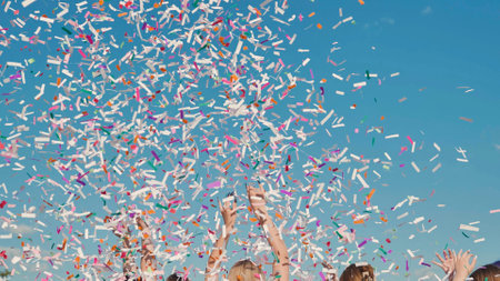 High school graduates joyfully throwing vibrant confetti in celebration against a clear blue skyの写真素材
