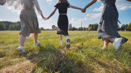 Three teenagers running and holding hands in a meadow, savoring their summer breakの写真素材