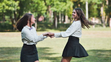 Two delighted schoolgirls twirling and holding hands in the park on their exciting first day back at schoolの写真素材