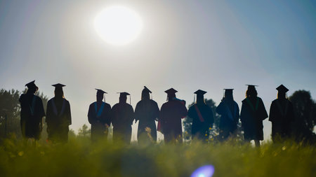 Graduates in cap and gown stand in a field at sunset, commemorating their high school graduation