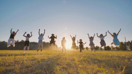 Friends happily leaping in a field, outlined against the golden light of the setting sun, commemorating their graduationの写真素材