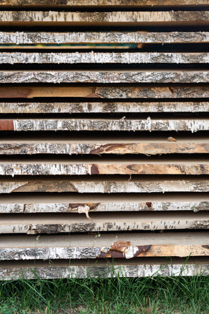 Wooden planks stacked horizontally, displaying raw birch bark texture, prepared for carpentry and...
