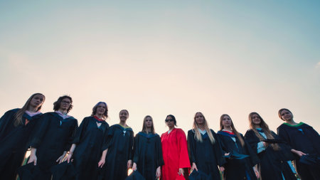 Students in graduation gowns celebrate their achievement by tossing their caps into the airの写真素材