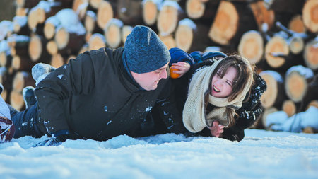 Father and daughter having fun lying on the snow and playing with a tangerine, in a winter day near...
