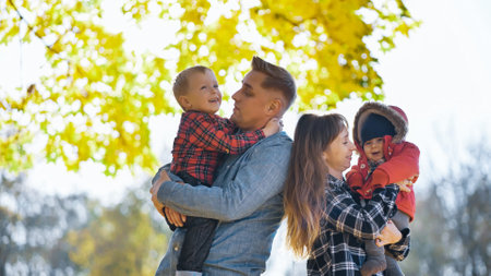 Parents holding their two children in a park, enjoying the beautiful fall foliage on a sunny autumn dayの写真素材