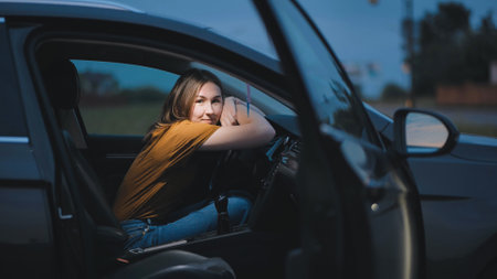 Peaceful female driver leaning on steering wheel, relaxing inside open door vehicle, seeking calm during quiet breakの写真素材