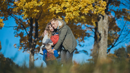 Family with two children enjoying a beautiful autumn day in a park, surrounded by colorful foliage and blue skyの写真素材