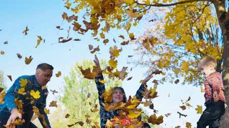 Family playing with dry leaves, laughing and bonding during sunny autumn day in park, sharing warm outdoor moments togetherの写真素材