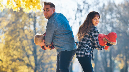 Family playing happily amid golden autumn foliage, parents spending precious moments with young kids in sunlit park landscapeの写真素材